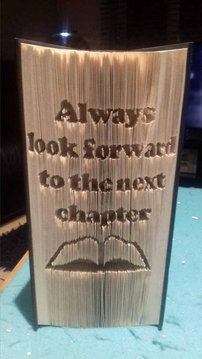 thick closed book, with dark cover, the phrase always look forward to the next chapter, carved into the pages, above the shape of an open book