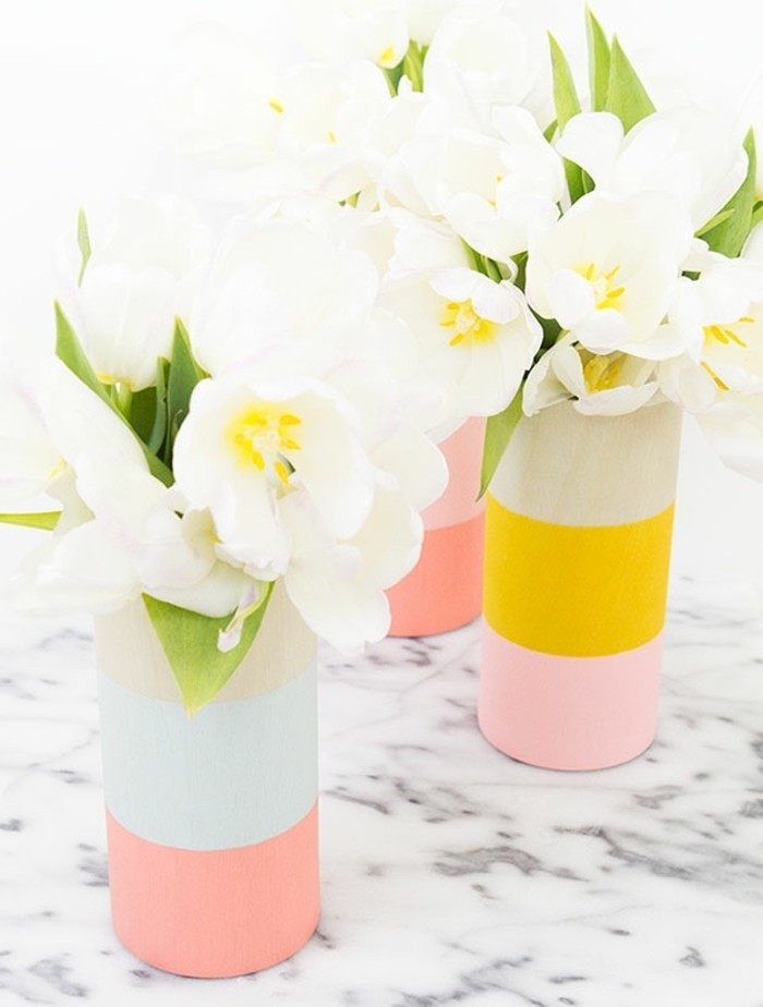 flower vases painted in pastel pink, pale blue and vivid yellow, a set of three, placed on marble surface, and containing white tulips