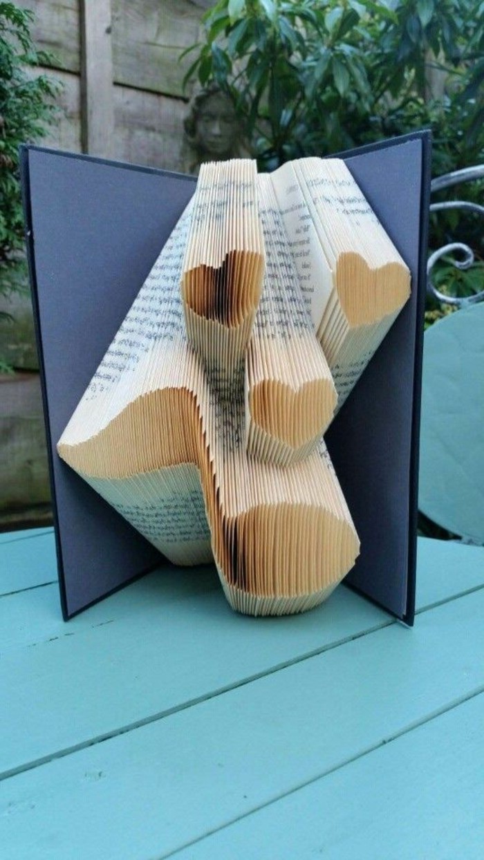 three hearts and a musical note, made from folded pages, inside an open book, with dark blue hard covers