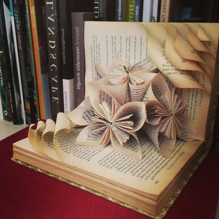 opened book, containing three flowers made from its pages, several other pages with rolled edges 