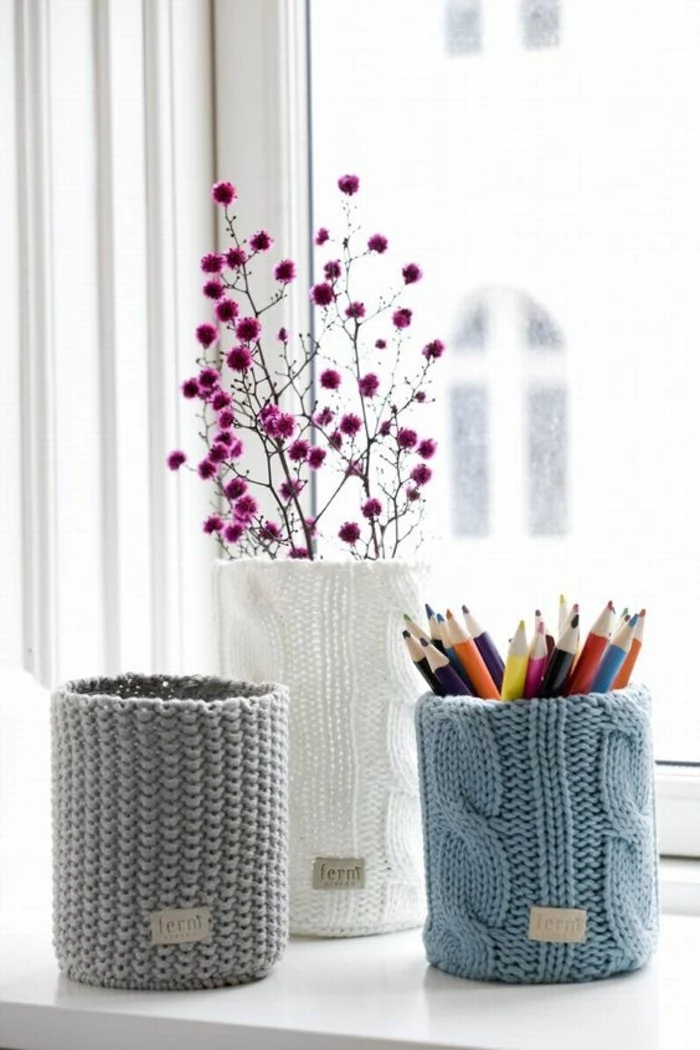 tin cans for crafts, three can knitted pencil holders in grey, white and light blue, containing colored pencils, and a dried purple plant