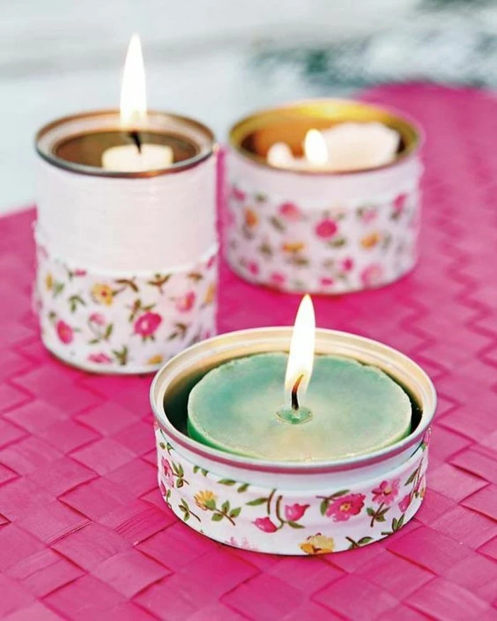 empty tin cans, three differently sized cans, painted white and decorated with floral paper, containing lit colors in different colors
