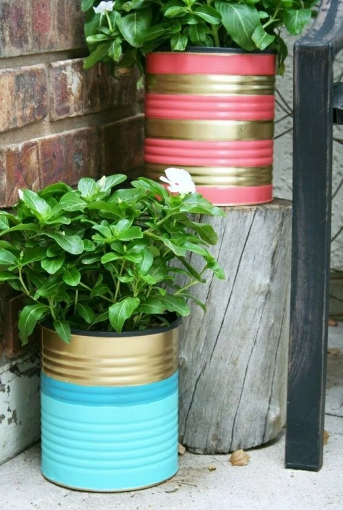 aluminum tins, two cans decorated with blue, pink and gold paint, containing green potted plants