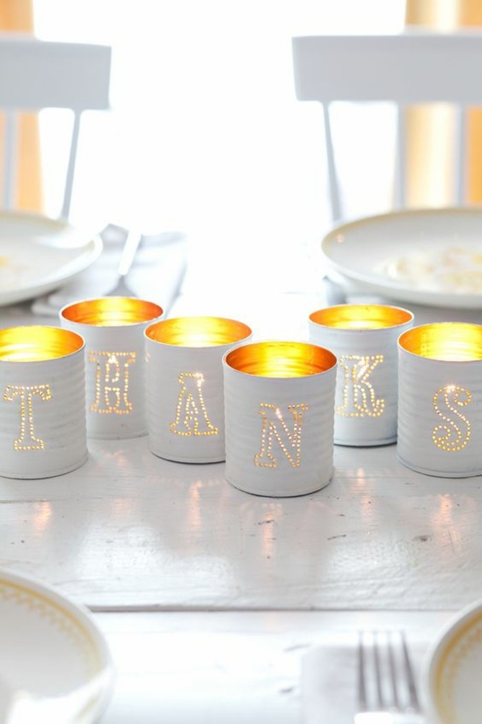six luminaries made from cans, painted white and containing lit candles, with holes shaping different letters on each can, placed so as to form the word thanks