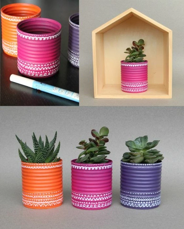 empty tin cans, three cans painted in orange, pink and violet, decorated with white marker, containing different succulents, pink can placed in wooden box