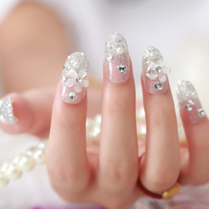 hand with clear nails, decorated with white acrylic flowers, silver rhinestones and glitter, holding pearl necklace