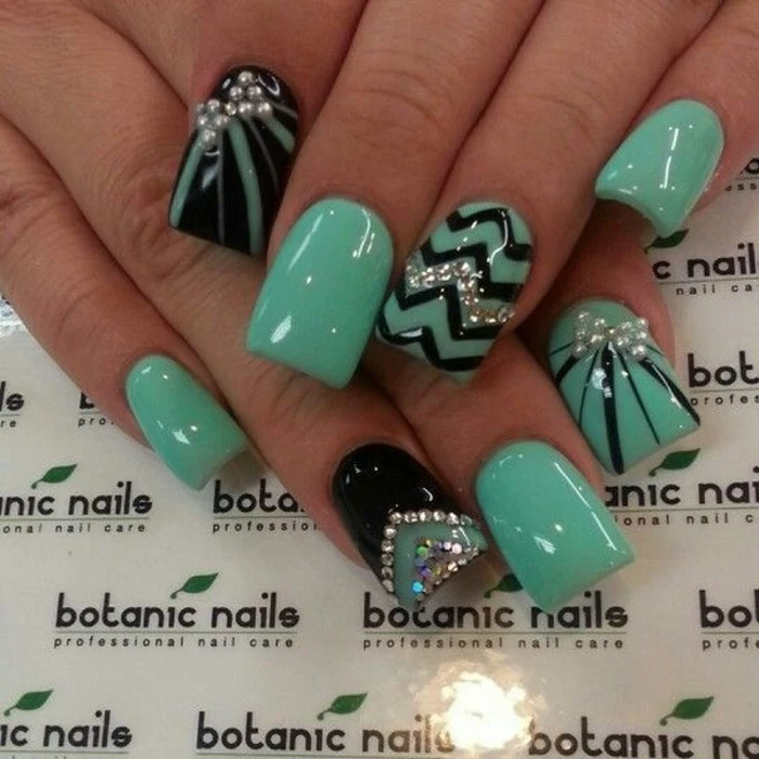 eight fingernails painted in turquoise green, with black details and rhinestone decorations
