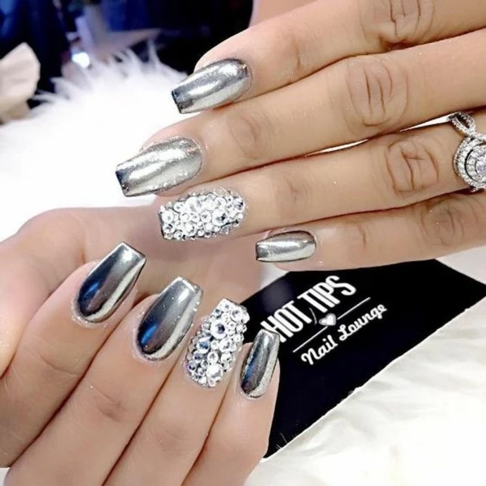 eight nails painted in shiny, metallic silver polish, ring fingers' nails covered in silver rhinestones