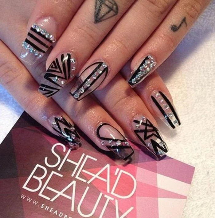close up of two hands with finger tattoos, decorated with clear fake nails, with rhinestones and black details