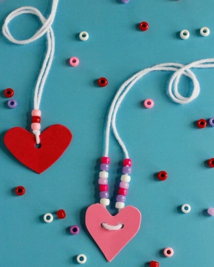 two heart-shaped felt cutouts in pink and red, attached to necklaces made of white string, decorated with pink, white and violet beads