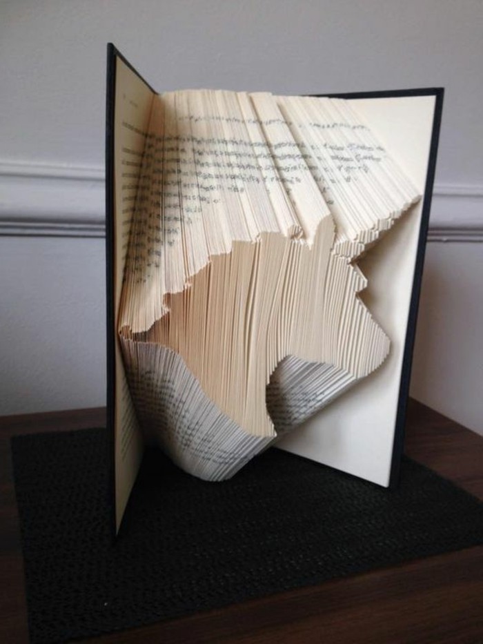 a unicorn head, made from folded pages, inside an open book, with dark hard covers