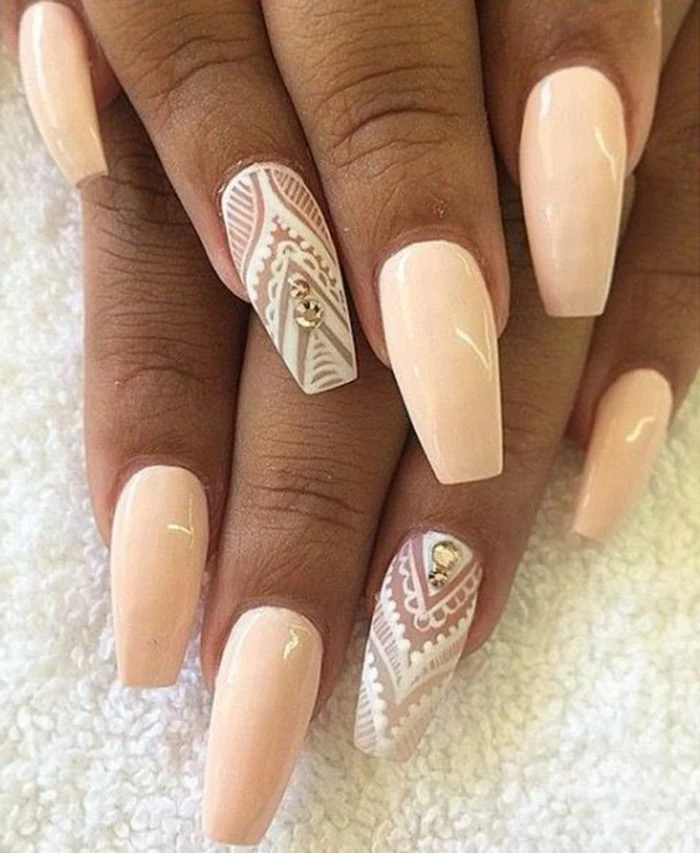 tan hands with pale peach-colored nail polish, ring fingers' decorated with rhinestones, and painted over with white figures