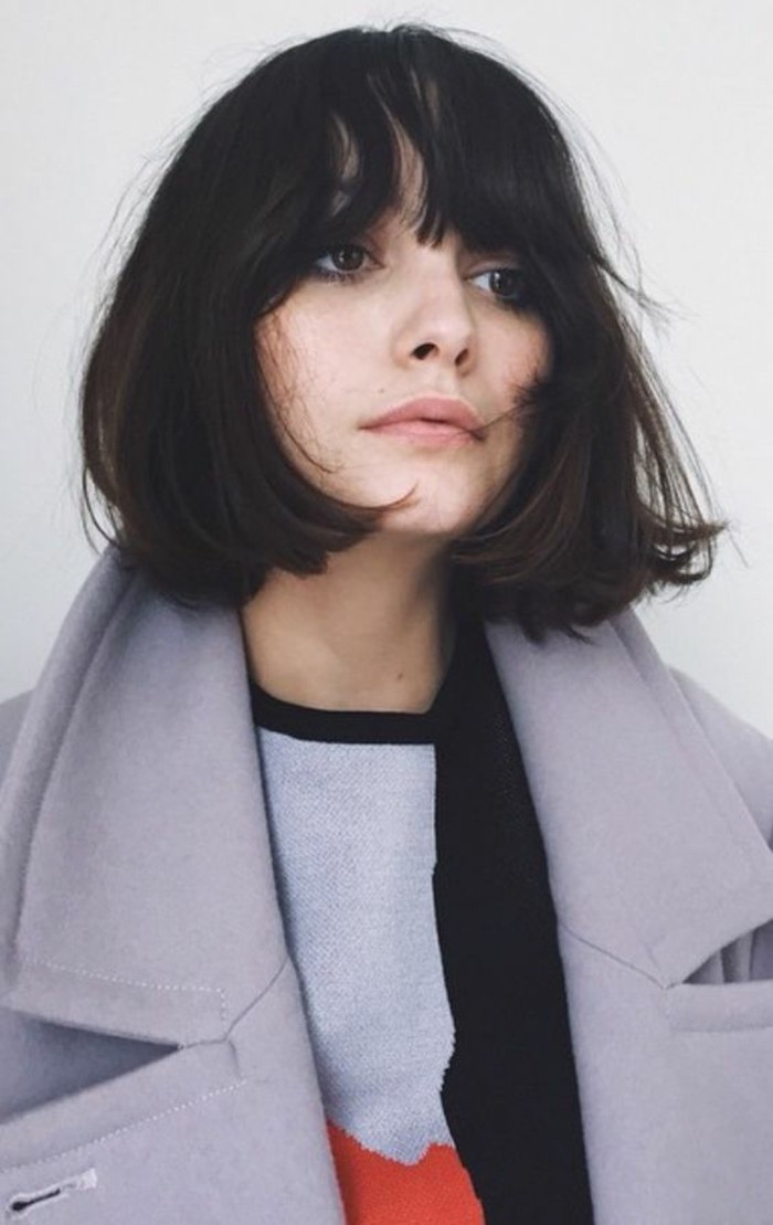 cute short haircuts, woman with messy black, chin-length hair and bangs, wearing big grey woolen coat, and colorful sweater
