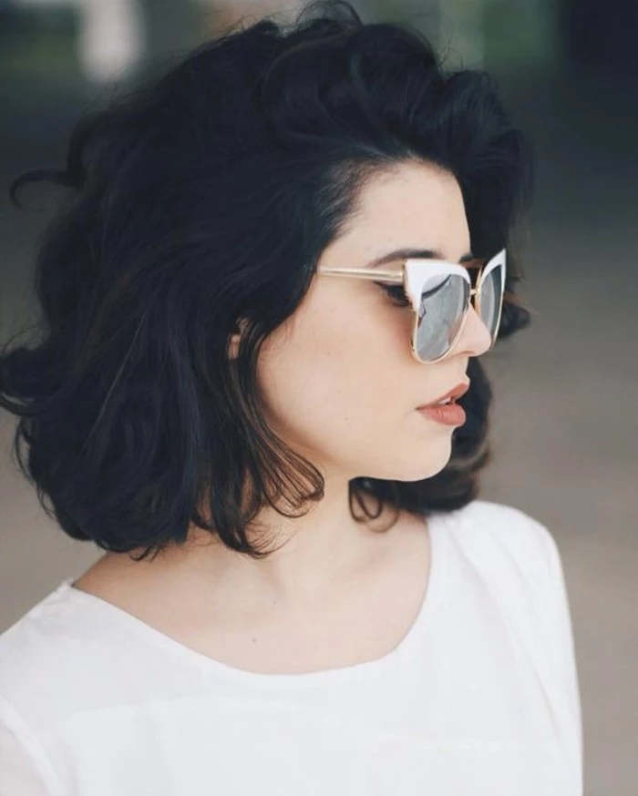 cute short haircuts, woman with short voluminous black wavy hair, wearing white top, and retro sunglasses with white frames