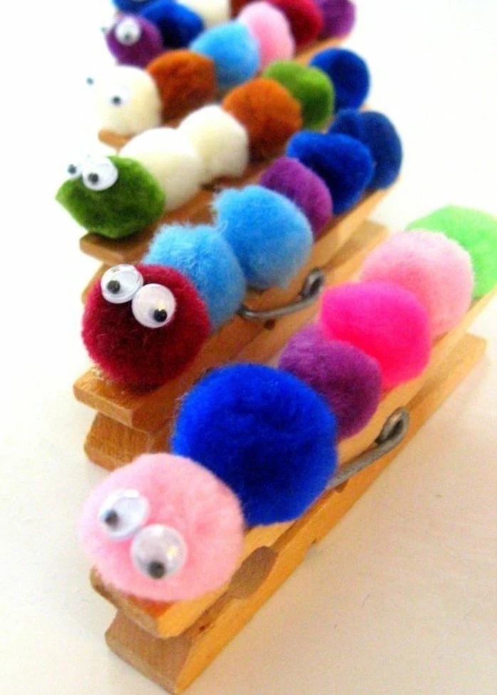 several wooden clothes pegs, with pom poms in different colors, decorated with googly stick-on eyes, looking like caterpillars