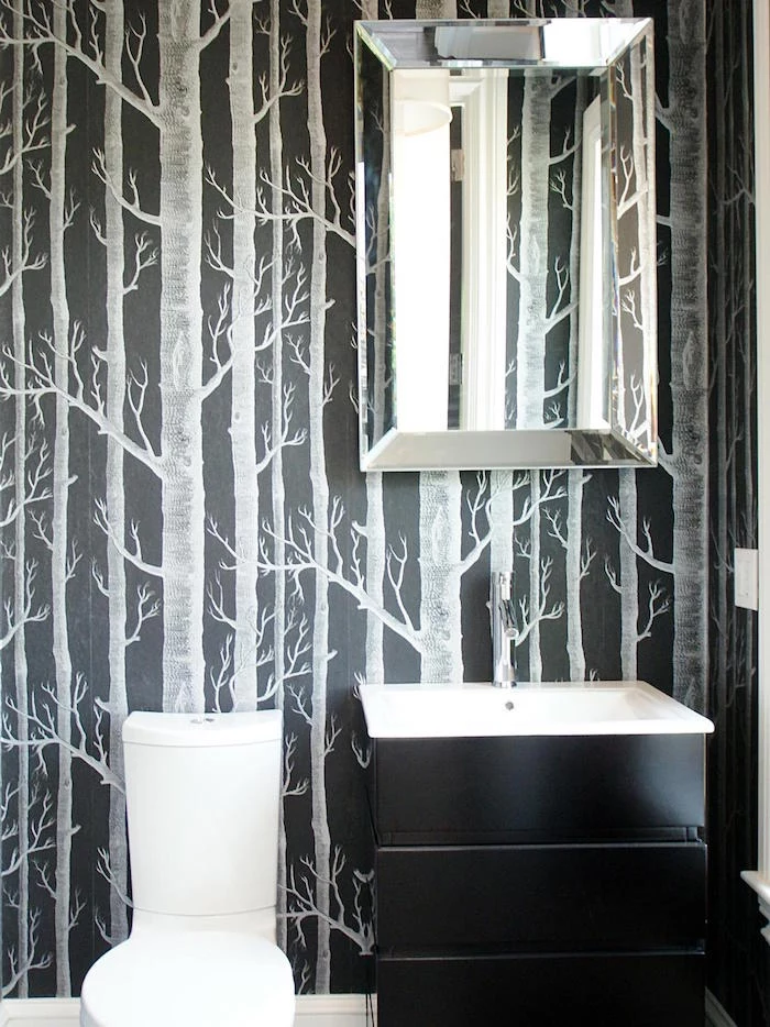 bathroom remodeling, dark wallpaper decorated with light grey painted leafless trees, modern white toilet seat, and a black chest of drawers with a white sink