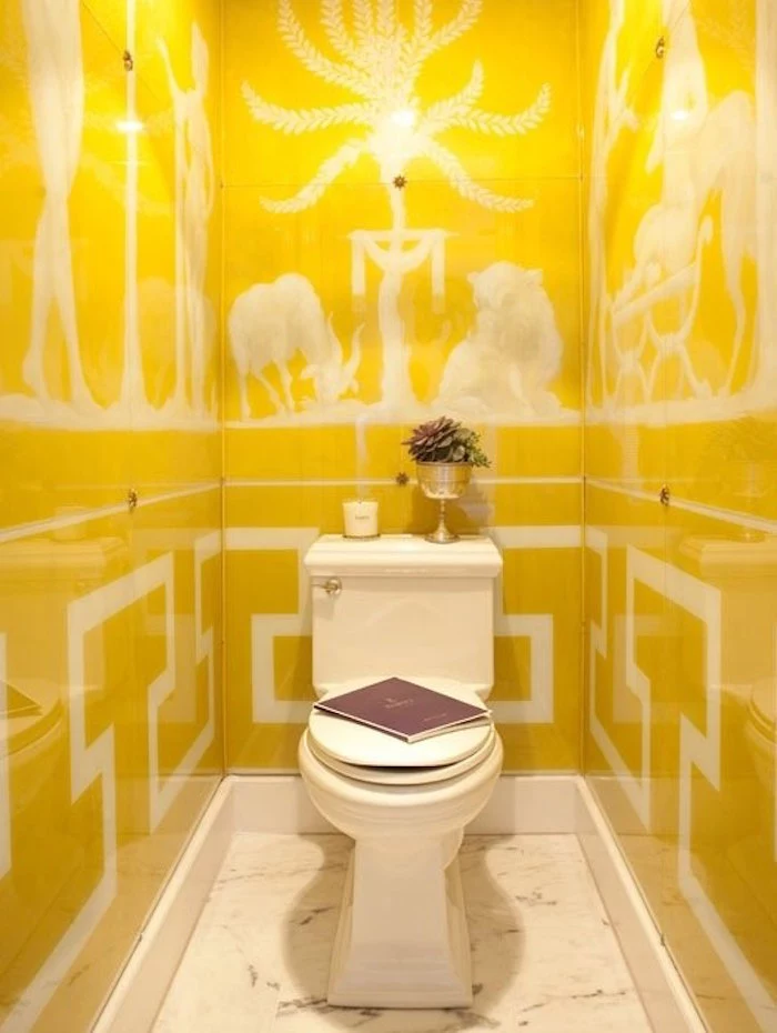 bathroom remodeling, narrow toilet with vintage white toilet seat, with flower vase, book and candle, walls covered with yellow panels, containing white drawings in Ancient Roman style