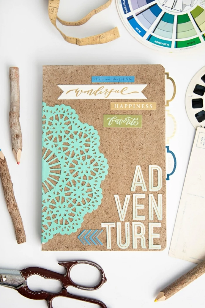journal with cork cover, decorated with cutouts, paper letters and a pale blue doily, diy craft projects, pencils made of rough wood and, other small items