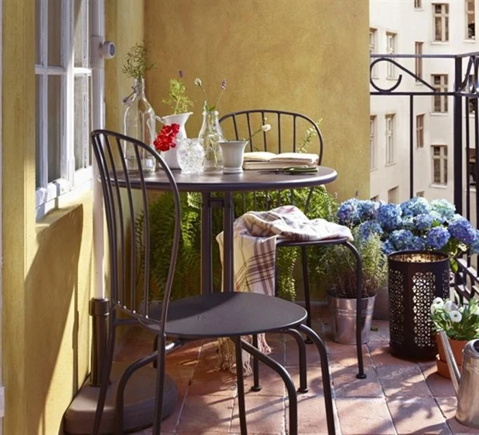 black round table with two matching chairs, near yellow wall, potted plants and black railing, porch décor