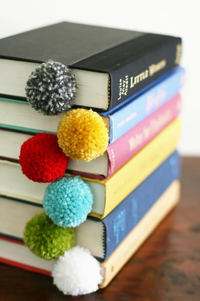 a stack of six books, with differently colored hard covers, containing dividers, decorated with differently colored pom-poms, diy craft projects
