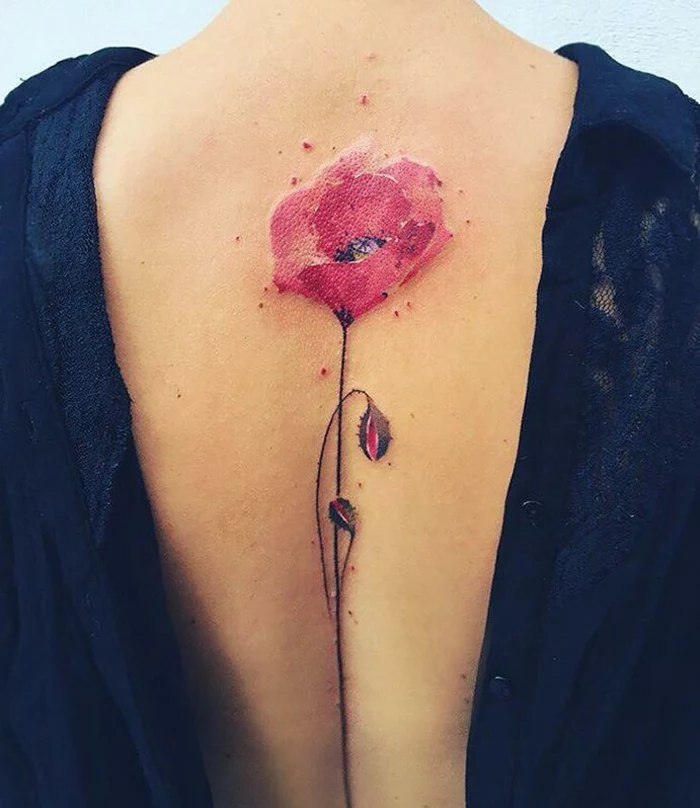 close up of a woman's back, with a water-color effect tattoo of a red poppy, with a thin green stalk and two buds