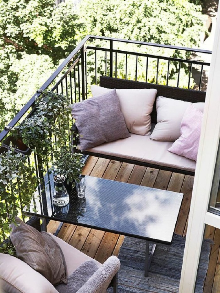 tiny terrace with black metal railing, with brown and pink settee and matching chair, both decorated with pink cushions, front porch decorating ideas, black rectangular table and rug