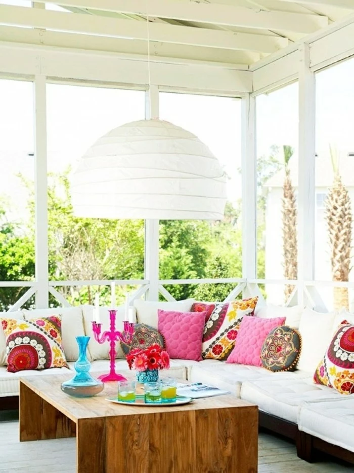 covered patio ideas, wooden table with many, bright colored decorative objects, large white and brown corner sofa, with many cushions in different shapes and colors, large white chandelier