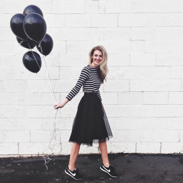 casual clothes, smiling woman with black and white striped top, black tulle skirt, and black and white sneakers, holding six black balloons