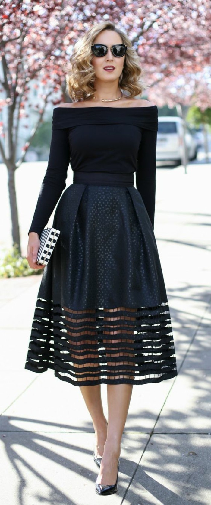 dress attire, blonde woman with shoulder-length curly hair and sunglasses, wearing black off-shoulder sweater, and black embellished skirt, with thick see-through lace hem