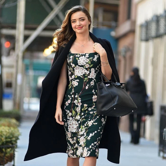 casual clothes, smiling miranda kerr, wearing a black coat over her shoulders, with dark green floral patterned dress, and black leather bag