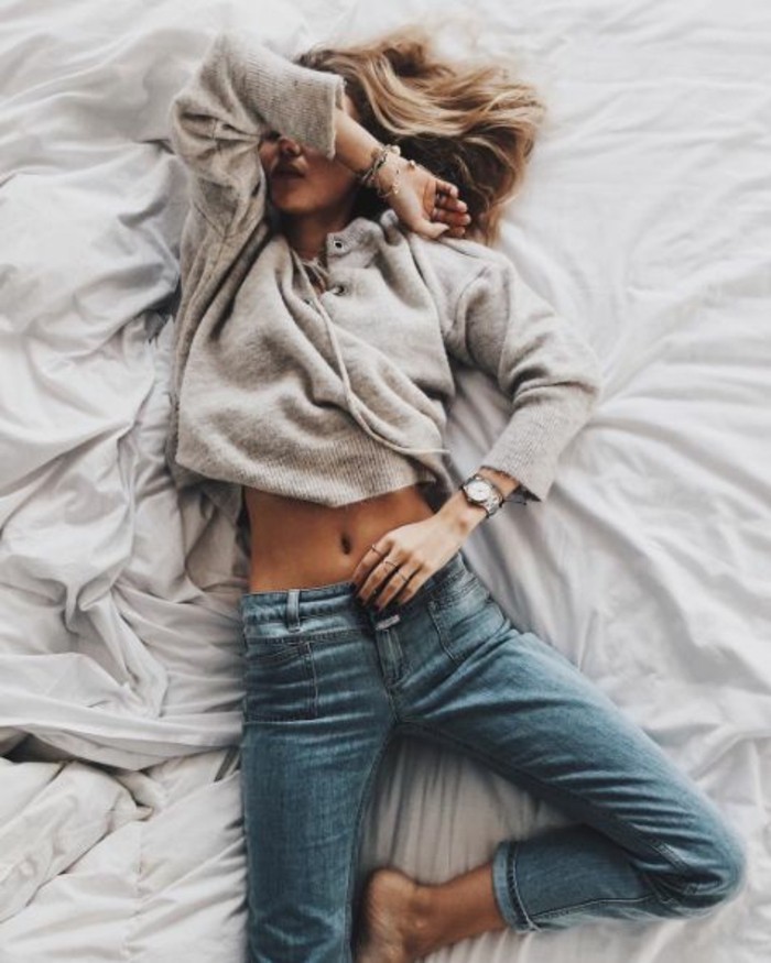 soft pale grey sweater with lace detail, and skinny pale blue ankle jeans, worn by blonde woman lying in bed, with an arm over her face