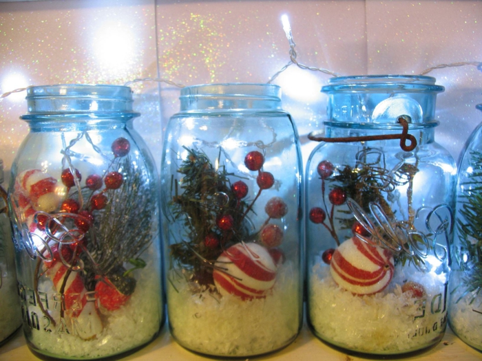 christmas mason jars, three jars containing fake snow, red berries and fir twigs, and red and white christmas ornaments