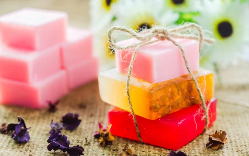 three handmade soaps, red orange and pink, stacked on top of each other, and tied with string, homemade crafts, more pink soaps in background