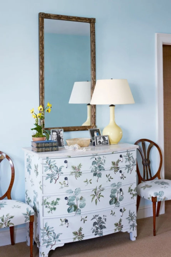 white chest of drawers, decorated with green plants decoupage, near two chairs with similar pattern, diy craft projects, large mirror and lamp