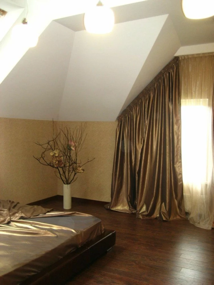 bedroom with white walls and cream paneling, bed with shiny, pale brown metallic cover, window with matching drapes, and sheer cream curtains