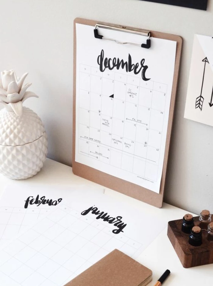 beige clip board, with white paper, showing a calendar, with the word december, written in fancy black writing, fun and easy crafts, white desk with stationary