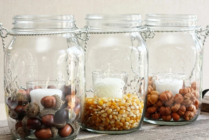 decorating mason jars, three jars with twisted wire handles, each containing a white candle in a glass, and either acorns, corn or micro pumpkins