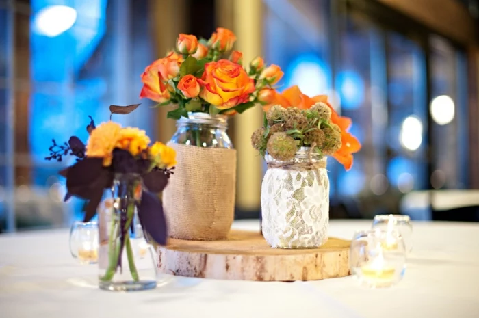 mason jar gifts, three jars either decorated with burlap, lace or kept plain, placed on a table, and containing various flowers in orange and yellow