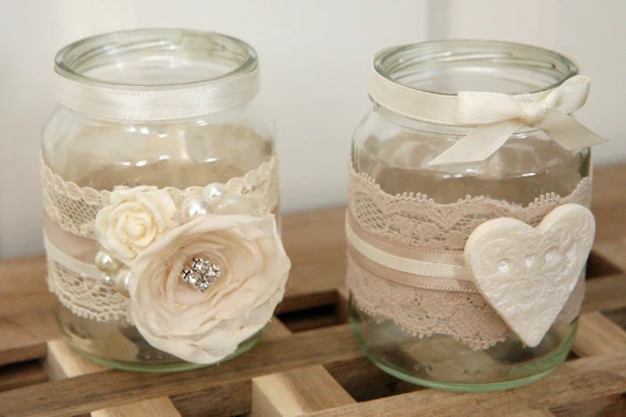 mason jar gifts, two small clear jars, with white lace, ribbons, faux flowers and a heart ornament stuck to them