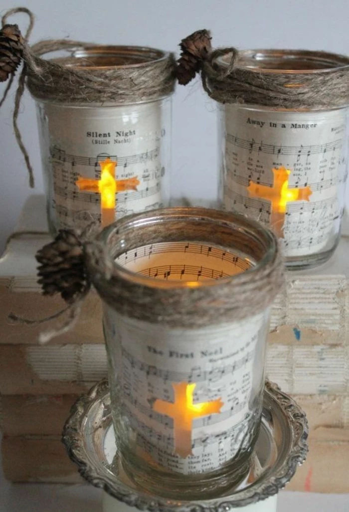 christmas mason jars, three jars decorated with sheet music, and tiny fir cones tied with string, a cross-shaped window reveals, a lit candle in each jar