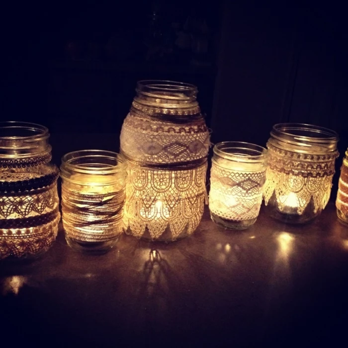 mason jar decorations, several differently sized jars, decorated with lace in different patterns, placed in a dark corner, and lit from within