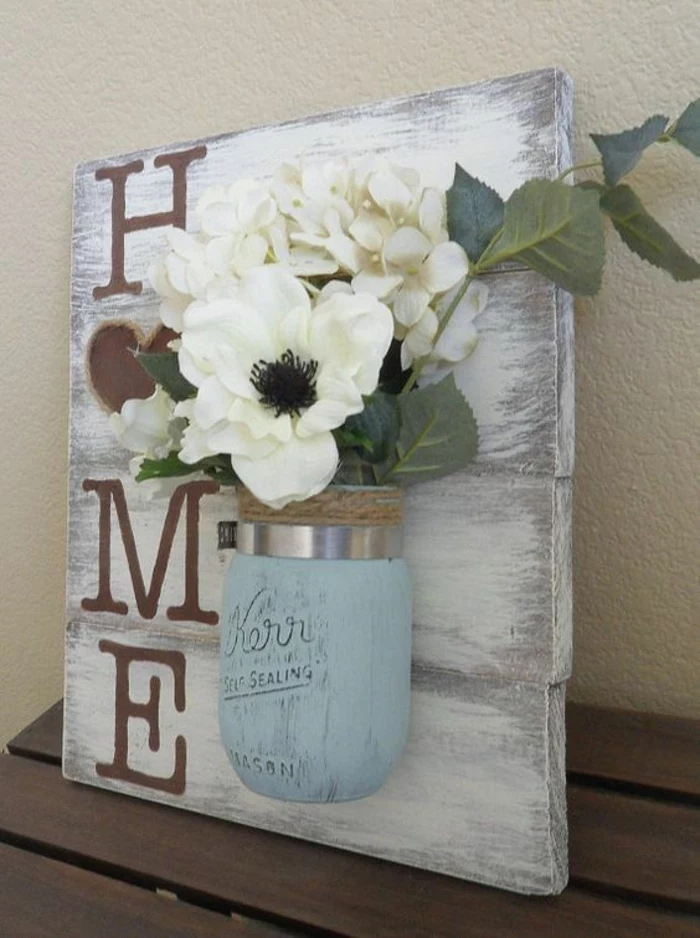 decorating mason jars, off-white wooden board, with the word home written in beige, decorated with a pale blue jar, containing faux white flowers