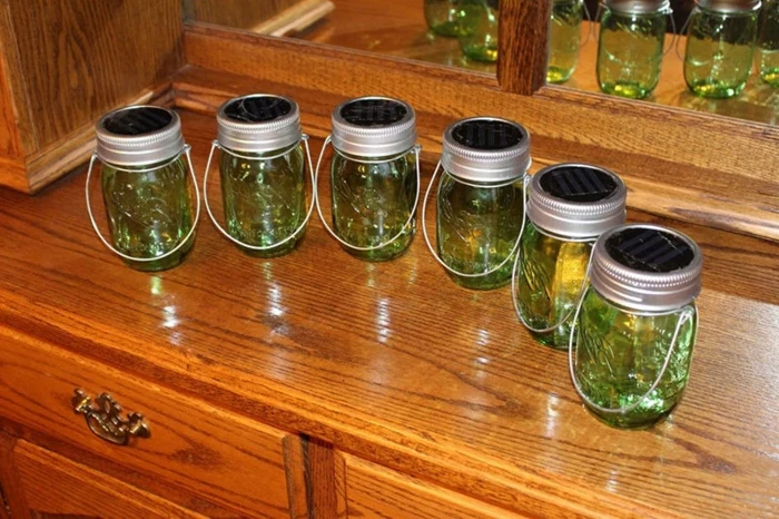 six mason jars, with aluminium lids and wire handles, containing clear green liquid, and placed on a wooden cupboard with mirror