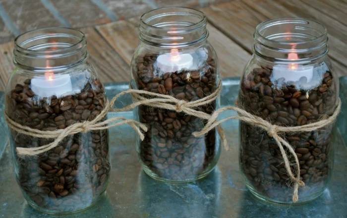 decorating mason jars, three jars filled with coffee beans, and decorated with string forming a bow, each containing a lit electric candle