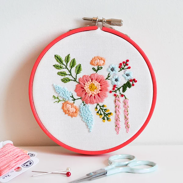 embroidery hoop with white fabric inside, decorated with cross-stitched flowers, art and craft ideas, scissors and pins, pink thread