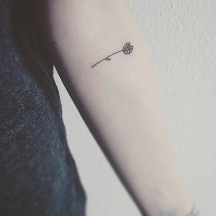 minimalistic and tiny, child-like image, of a daisy-like flower, tattooed on a person's lower arm, with black ink