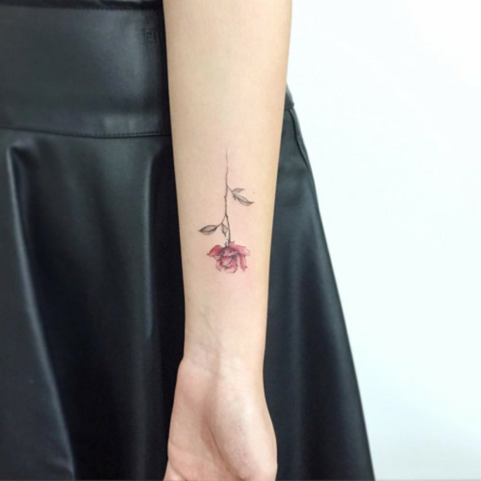flower tattoos, slim female arm, with soft and small minimalist tattoo, depicting a red rose on a pale green stalk, black leather skirt in background
