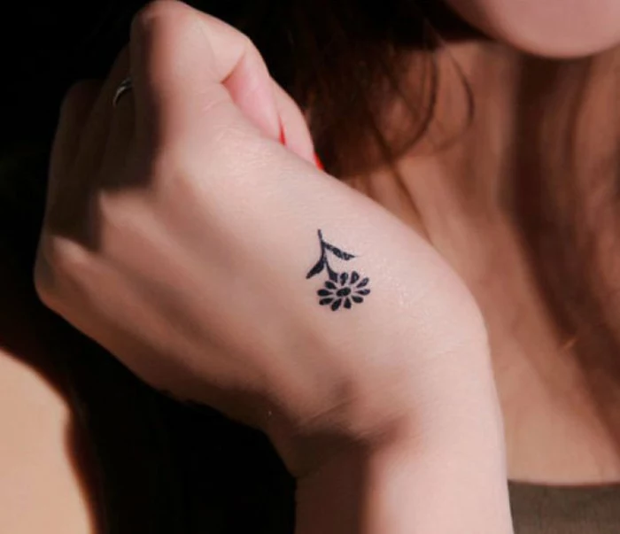 flower tattoos, close up of a hand, with a tiny minimalist tattoo, depicting a simple daisy, made with black ink