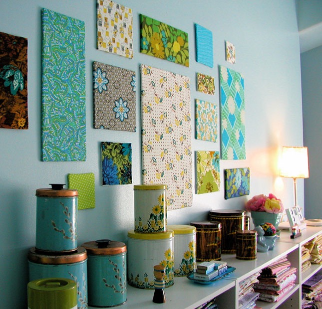 blue wall of a room, with many differently-sized canvases, decorated with various, multicolored patterns, shelf with many different items nearby