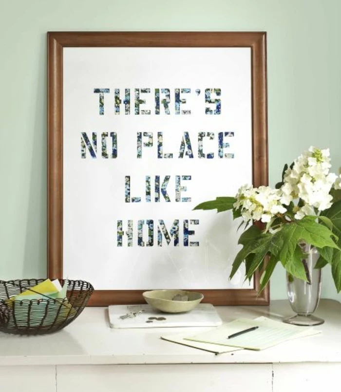 framed sheet of paper, with the words there's no place like home, homemade crafts, placed on a desk, near vase with flowers and stationary